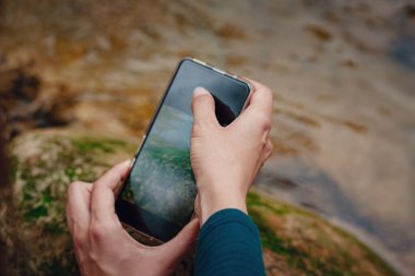 Dağ nehrinde akıllı telefonla fotoğraf çeken bir kadın yürüyüşçü. Gadget konsepti. Seyahat kavramı.