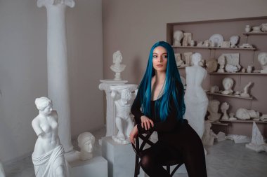 Beautiful young girl with blue hair in skinny black at the working place in the old atmospheric studio. sitter model, muse and inspirer concept clipart