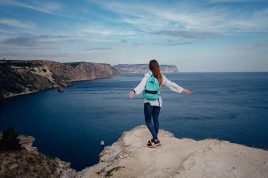 Soğuk denizin üzerindeki uçurumda yalnız bir kadın. Seyahat yaşam tarzı konsepti. Yalnızlık melankolik duygular. Turistler mavi güneş okyanusuna bakar, yaz yaşam tarzına