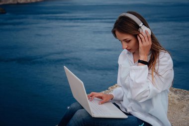 Plajda, kayalıklarda çalışan genç bir iş kadını. Teknoloji ve seyahat. Açık havada çalışmak. Serbest konsept.
