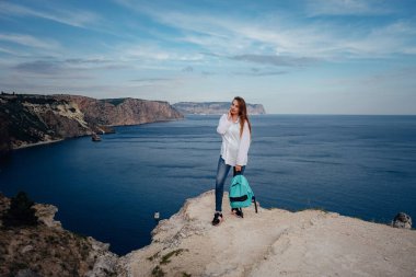 Soğuk denizin üzerindeki uçurumda yalnız bir kadın. Seyahat yaşam tarzı konsepti. Yalnızlık melankolik duygular. Turistler mavi güneş okyanusuna bakar, yaz yaşam tarzına