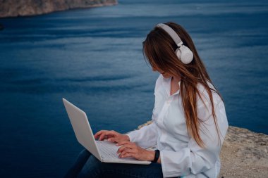 Plajda, kayalıklarda çalışan genç bir iş kadını. Teknoloji ve seyahat. Açık havada çalışmak. Serbest konsept.
