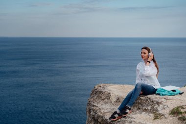 Plajda, kayalıklarda çalışan genç bir iş kadını. Dağın tepesinde, deniz kenarında bir dizüstü bilgisayarda çalışan, şekil değiştiren genç bir kız..