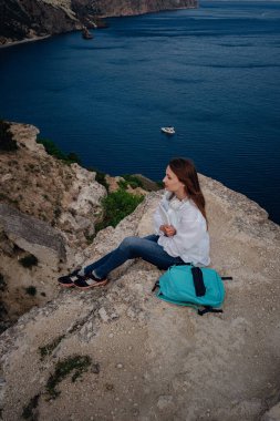 Plajda, kayalıklarda çalışan genç bir iş kadını. Teknoloji ve seyahat. Açık havada çalışmak. Serbest konsept.