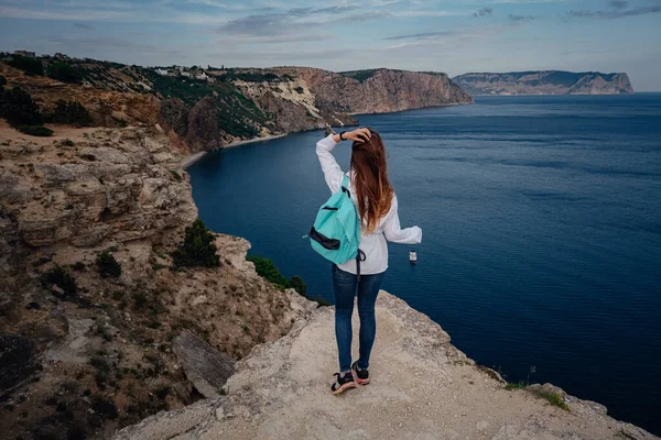 Woman above cold sea on cliff alone. Travel Lifestyle concept outdoor. Solitude melancholy emotions. Tourist look on blue sun ocean, summer lifestyle