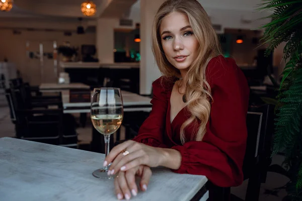 カフェやレストランで白ワインを飲む女性です セクシーな若いブロンドの女の子 お祝いとかお酒とかスタイルとかファッショナブルなライフスタイルとか 肖像画の女の子で赤ドレスでワイングラス — ストック写真
