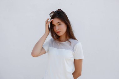 Beyaz tişört ve kot pantolon giyen hippi kadın sokak duvarına karşı poz veriyor, minimalist kentsel giyim tarzı, tişört baskısı mağazası için model.