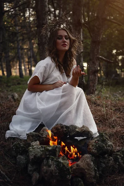 秋天森林里穿着白色长裙的美丽神秘哥特式女人 黑暗的幻想生物 巫婆正坐在炉边 — 图库照片