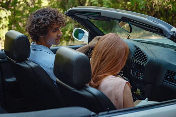 Couple enjoying a drive in a convertible in summer road. Friends going on holidays. Italian vacation serpentine roads, a redheaded woman and a beautiful young man