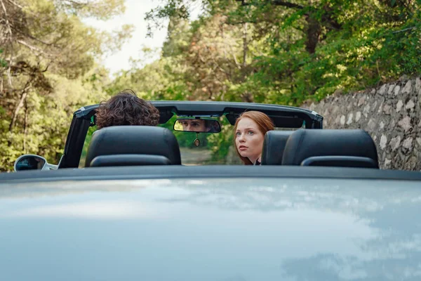 Couple enjoying a drive in a convertible in summer road. Friends going on holidays. Italian vacation serpentine roads, a redheaded woman and a beautiful young man