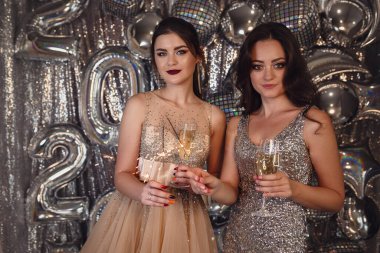 Güzel, ince, parlak makyajlı, gümüş renkli arka planda elbisesi olan genç bir kadın. Parti fotoğrafı, gümüş konfeti, disko topu. Yılbaşı partisinde eğleniyorum. Tatil Kutlaması