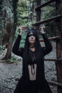 Gizemli büyücü kadın cadı karanlık ormanda güzel siyah elbise yürüyüşü. Gotik görünüşlü kadın. Cadılar bayramı için uygun.