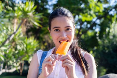 Kot pantolon ve beyaz tişörtlü at kuyruklu kız çocuk gibi parkta portakallı dondurmayı ısır..
