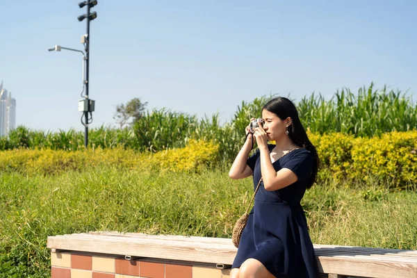 公園のベンチに座ってカメラで写真を撮る暗い青のドレスの長い髪の女性 — ストック写真