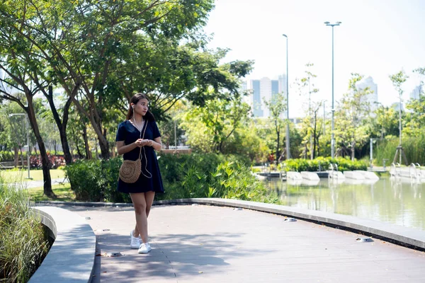 公園内に噴水のある池の横を一人で歩いている濃い青のドレスの長い髪の女性 — ストック写真