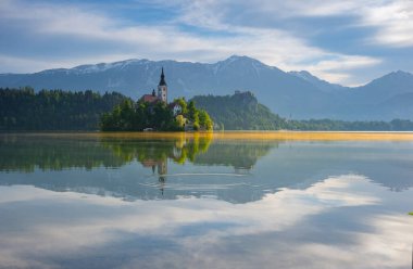 Bled Gölü 'nde güzel bir sabah ve arka planda Julian Alps. Göl adası ve Mary 'nin Varsayımına adanmış küçük sevimli kilise Slovenya' daki ünlü turistik merkezlerdir.