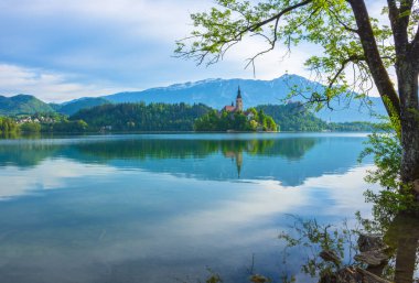 Bled Gölü 'nde güzel bir sabah ve arka planda Julian Alps. Göl adası ve Mary 'nin Varsayımına adanmış küçük sevimli kilise Slovenya' daki ünlü turistik merkezlerdir.