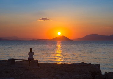 Yunanistan 'ın Saronik Körfezi' ndeki Aegina adasından Akdeniz üzerinde gün batımını izleyen kız silueti.
