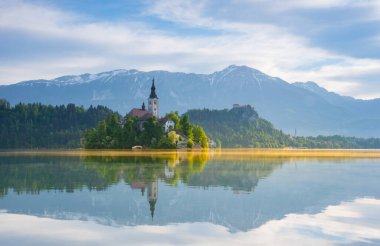 Bled Gölü 'nde güzel bir sabah ve arka planda Julian Alps. Göl adası ve Mary 'nin Varsayımına adanmış küçük sevimli kilise Slovenya' daki ünlü turistik merkezlerdir.