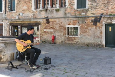 Venedik, İtalya - 20 Nisan 2019: Genç sokak sanatçısı eski bir meydanda gitar çalıyor