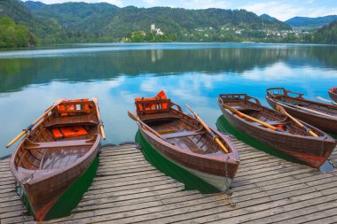 Gölde turistleri bekleyen geleneksel tekneler Bled Gölü 'nde, arkada küçük sevimli bir kilise ve Slovenya' nın ünlü turistleri.