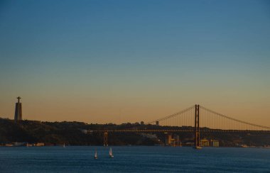 25 Nisan 'da Tagus nehri üzerindeki asma köprü ve Lizbon, Portekiz' deki İsa heykeli üzerinde gün batımı.