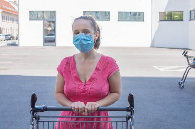 Coronavirus Covid-19 salgını sırasında elinde alışveriş arabasıyla bir mağazanın önünde duran tıbbi maske takan bir kadın..