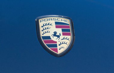 Porsche logosu mavi bir arabaya yakın.