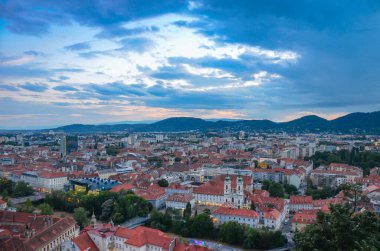 Avusturya 'nın Styria bölgesindeki Mariahilfer kilisesi ve tarihi binalarıyla Graz şehrinin üzerinde bulutlu bir gün batımı var.