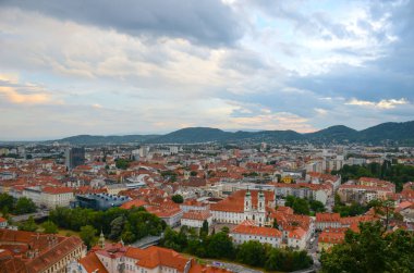 Avusturya 'nın Styria bölgesindeki Mariahilfer kilisesi ve tarihi binalarıyla Graz şehrinin üzerinde bulutlu bir gün batımı var.