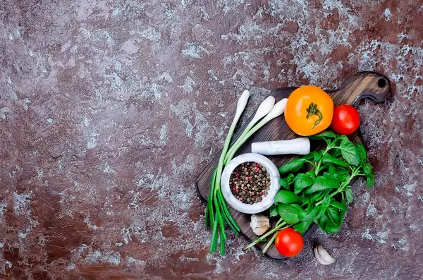 Olgun kırmızı ve sarı domates, yeşil soğan ve fesleğen, sarımsak, tuz ve baharat karanlık bir taş zemin üzerine. Üstten görünüm, kopya alanı. 