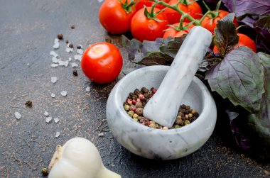 Bir taş harç ve bir sürü yeşil ve kırmızı fesleğen ve olgun domates, sarımsak, baharatlar tuz karanlık bir taş arka plan üzerinde. Üstten görünüm, kopya alanı.