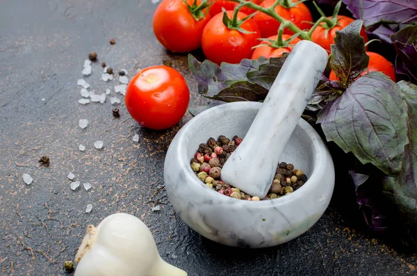 Bir taş harç ve bir sürü yeşil ve kırmızı fesleğen ve olgun domates, sarımsak, baharatlar tuz karanlık bir taş arka plan üzerinde. Üstten görünüm, kopya alanı.