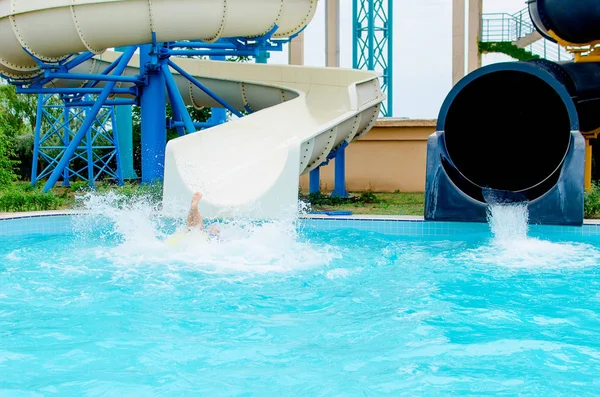 白人の子は水スライド ダウンした後プールに落ちる 多くの水スプレー 足のみが表示されます 水公園の概念と夏休み — ストック写真