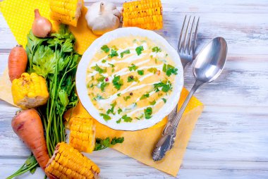 Ev yapımı Mısır krem çorbası ekşi krema, beyaz bir tabak ve dilim kızarmış Mısır koçanı Beyaz ahşap bir masa üzerinde otlar. üstten görünüm, kopya alanı 