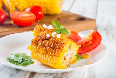 Lezzetli Barbecued Mısır koçanı otlar, sebzeler ve tuz beyaz bir tabak ve beyaz bir ahşap masa