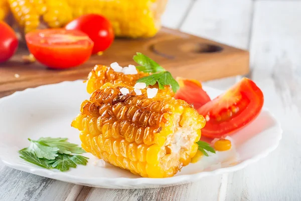 Lezzetli Barbecued Mısır koçanı otlar, sebzeler ve tuz beyaz bir tabak ve beyaz bir ahşap masa