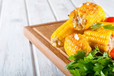 Lezzetli Barbecued Mısır koçanı otlar, sebzeler ve tuz bir tahta ve bir beyaz ahşap masa