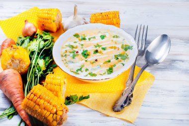 Ev yapımı Mısır krem çorbası ekşi krema, beyaz bir tabak ve dilim kızarmış Mısır koçanı Beyaz ahşap bir masa üzerinde otlar. üstten görünüm, kopya alanı 