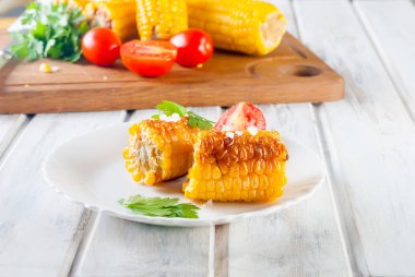 Lezzetli Barbecued Mısır koçanı otlar, sebzeler ve tuz beyaz bir tabak ve beyaz bir ahşap masa