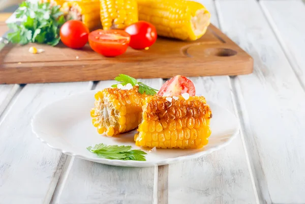 Lezzetli Barbecued Mısır koçanı otlar, sebzeler ve tuz beyaz bir tabak ve beyaz bir ahşap masa