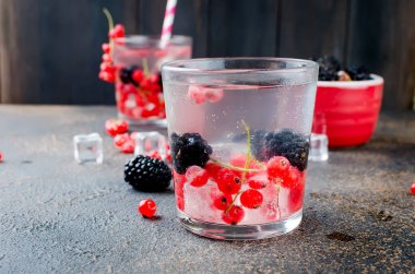 bir kokteyl ile iki bardak kırmızı kuş üzümü, blackberry ve buz ve karanlık bir arka plan kopya alanı üzerinde kase çilek