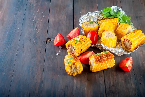 Tasty Barbecued corn cobs with herbs, vegetables and salt on a dark old wooden table