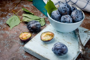 Bir çanak çömlek mavi kase bir erik taze mor Erik yarıya ve parlak meyve hamuru koyu kahverengi rustik arka plan üzerinde seçici odak, kopya alanı parlıyor 