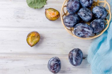 Taze mor erik erik bir hasır vazoda yarıya ve parlak meyve hamuru Beyaz ahşap zemin üzerinde kopya alanı parlıyor,