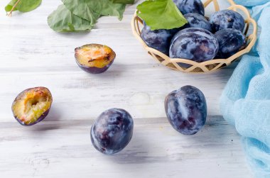 Taze mor erik erik bir hasır vazoda yarıya ve parlak meyve hamuru Beyaz ahşap zemin üzerinde kopya alanı parlıyor,