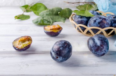 Taze mor erik erik bir hasır vazoda yarıya ve parlak meyve hamuru Beyaz ahşap zemin üzerinde kopya alanı parlıyor,