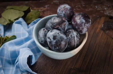 Bir seramik kase ve koyu kahverengi rustik arka plan seçici odak, kopya alanı yapraklarda mavi Erik 