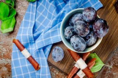 Kase taze mor Erik bir çömlek içinde mavi ve masanın üzerine dağılmış, erik meyve deri ve kuru cips şeklinde rulolar üzerinde koyu arka plan. Detoks kavramı. Sağlıklı gıda, meyve inanılmaz şeker. seçici odak, kopya alanı 