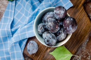 Bir seramik kase ve koyu kahverengi rustik arka plan seçici odak, kopya alanı yapraklarda mavi Erik 